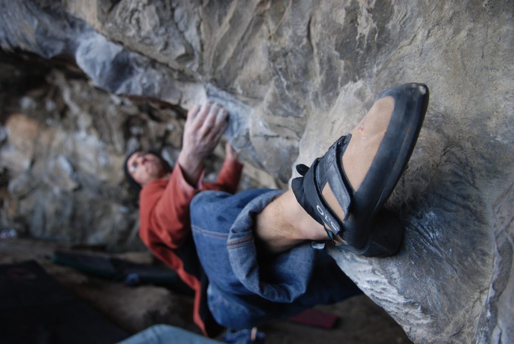 A climber heelhooking his way across the brutal Lou Ferrino, V9, Parisellas Cave, Great Ormes.